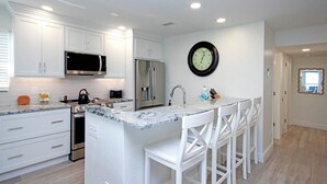 A modern kitchen with white cabinetry, a stainless steel refrigerator, a microwave, and a large island with bar stools. - Spectacular Unit C5 · Sanibel Arms West | Gulffront Endless Gulf Views (Sanibel)