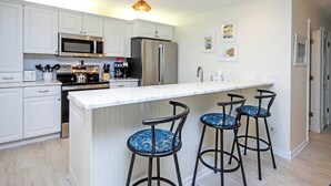 Eine moderne Küche mit weißen Schränken, Edelstahlgeräten und einer zentralen Kochinsel mit Barhocker.