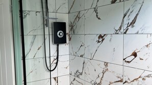 A bathroom with a glass-enclosed shower, a white bathtub, and marble-patterned tiles.
