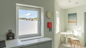A modern kitchen with a window, a clock, a fire blanket, and a small table with chairs.