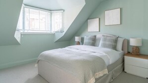 A bedroom with a sloped ceiling, a bed with white bedding, two bedside tables with lamps, and a window with blinds.