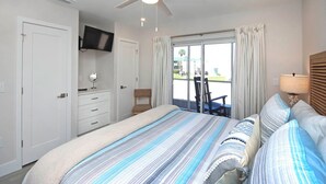 A bedroom with a bed, a ceiling fan, a TV mounted on the wall, a window with curtains, and a view of the outside. - Pristine Unit D1 Sanibel Arms West | Gulffront Panoramic Gulf Views (Sanibel)