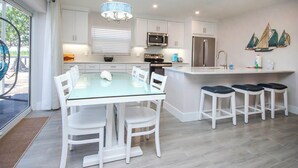 A modern kitchen with white cabinetry, stainless steel appliances, and a glass dining table with white chairs. - Pristine Unit D1 Sanibel Arms West | Gulffront Panoramic Gulf Views (Sanibel)