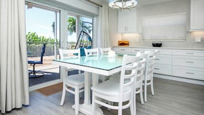 A modern kitchen with white cabinetry, a glass dining table, and a hanging light fixture. - Pristine Unit D1 Sanibel Arms West | Gulffront Panoramic Gulf Views (Sanibel)