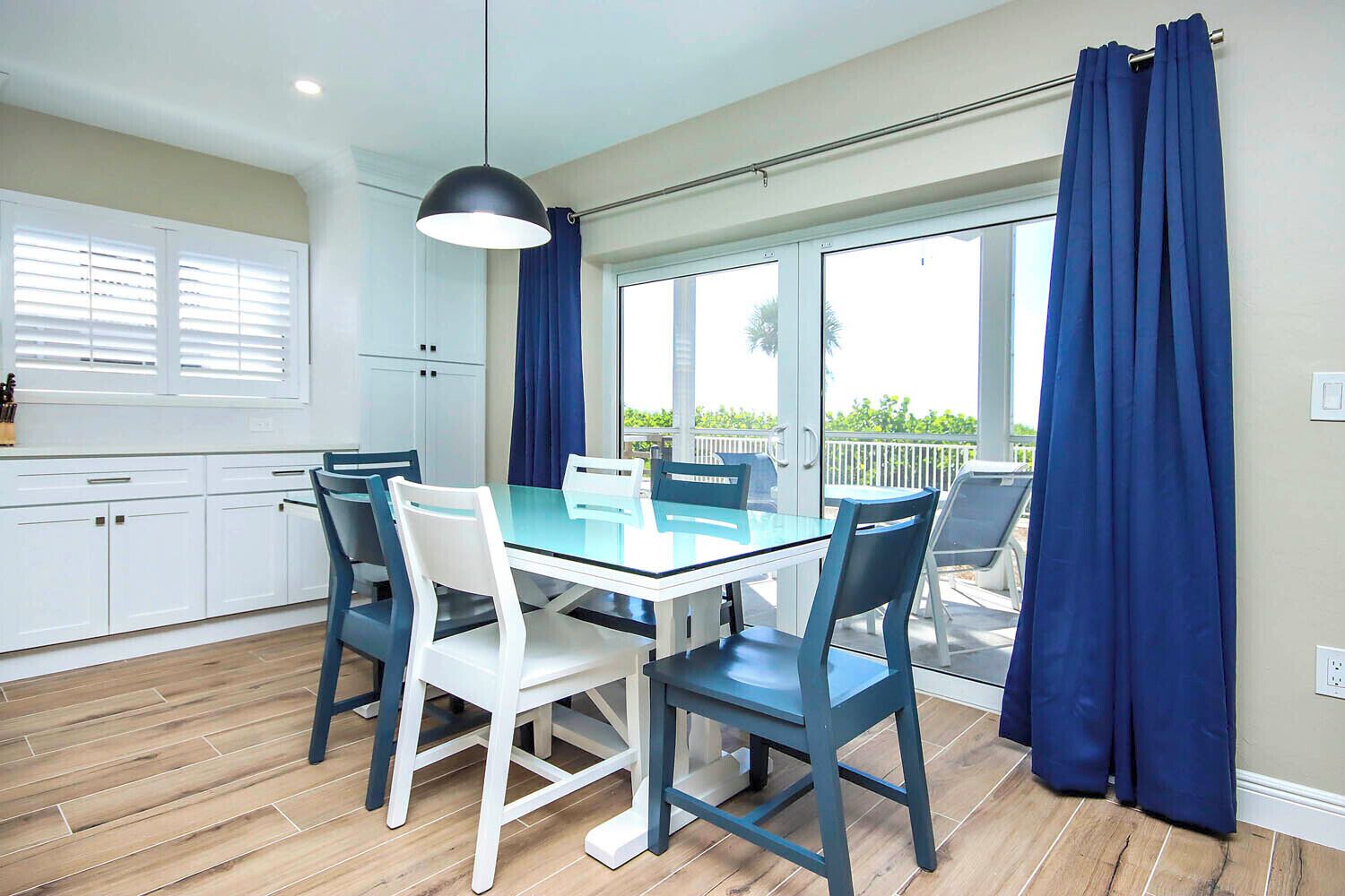 A dining area with a glass table and chairs, a pendant light, and a view through a sliding glass door to an outdoor patio.