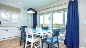 A dining area with a glass table and chairs, a pendant light, and a view through a sliding glass door to an outdoor patio. - Breezy Unit D4 · Sanibel Arms West | Gulffront Breathtaking Gulf Views (Sanibel)