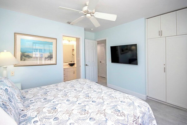 Ein Schlafzimmer mit Bett, Deckenventilator, Fernseher und Kleiderschrank.