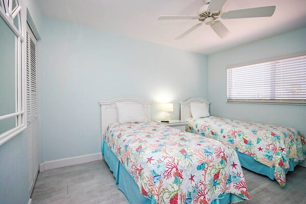 A bedroom with two beds, a ceiling fan, a nightstand with a lamp, and a window with blinds. - Relax in Peaceful Paradise Directly on the Beach (Sanibel)