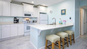 Une cuisine moderne avec des armoires blanches, un grand îlot central doté de tabourets, un four à micro-ondes, une cuisinière, un réfrigérateur et une horloge murale.