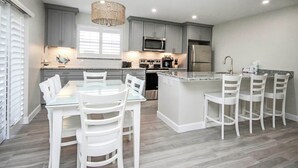 A modern kitchen with grey cabinets, stainless steel appliances, a glass dining table, and white chairs. - Mesmerizing Unit E1 · Sanibel Arms West | Gulffront Magnificent Gulf Views (Sanibel)