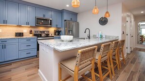 A modern kitchen with blue cabinets, a granite countertop, a built-in oven, a refrigerator, and a large island with bar stools.