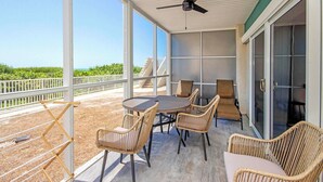A covered outdoor patio with a table and chairs, a ceiling fan, and a view of the ocean.