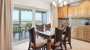 A dining area with a glass table and chairs, wooden cabinets, and a view of the ocean. - Breathtaking Unit E7 · Sanibel Arms West | Gulffront Stunning Gulf Views (Sanibel)