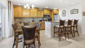 A kitchen with wooden cabinets, a granite countertop, a central island with bar stools, and a chandelier. - Breathtaking Unit E7 · Sanibel Arms West | Gulffront Stunning Gulf Views (Sanibel)