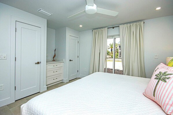 A bedroom with a bed, a dresser, a ceiling fan, and a window with curtains.