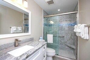 A modern bathroom with a marble countertop, a white sink, a glass-enclosed shower, and a toilet.