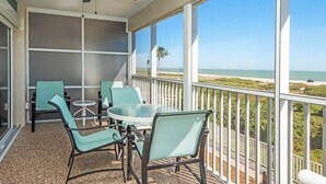 Een balkon met een tafel en stoelen, een plafondventilator en uitzicht op het strand.