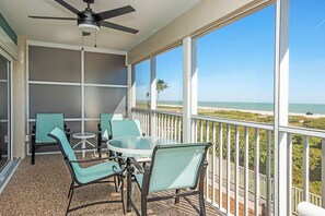 A balcony with a table and chairs, a ceiling fan, and a view of the beach. - Sanibel Beachfront Retreat/ Gulf Views/ Pool & Pickleball/ Bright & Updated (Sanibel)