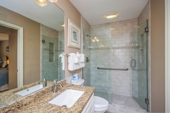 A modern bathroom with a double sink, glass shower enclosure, and a toilet.
