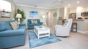 A living room with a sofa, armchair, coffee table, and a dining area with a chair and table.