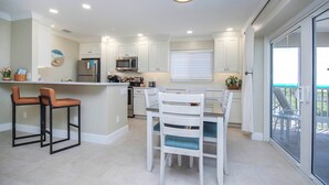 A modern kitchen with white cabinetry, a central island, and a dining area with white chairs.
