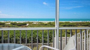 A balcony with a view of a beach, a table, and a chair.