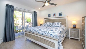 Un dormitorio con cama, ventilador de techo, mesita de noche, cómoda y ventana con cortinas.