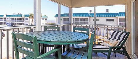 A balcony with a round table and chairs, a striped lounge chair, and a view of buildings in the background.