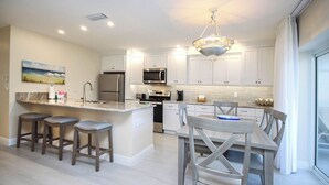 A modern kitchen with a central island, bar stools, a dining table with chairs, and a view of the outdoors. - Beautifully renovated desirable first floor Unit H-2 (Sanibel)