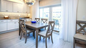 A modern kitchen with white cabinets, a wooden dining table, and a chandelier. - Beautifully renovated desirable first floor Unit H-2 (Sanibel)
