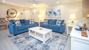 A modern living room with two blue sofas, a white coffee table, and a ceiling fan. - Beautifully renovated desirable first floor Unit H-2 (Sanibel)