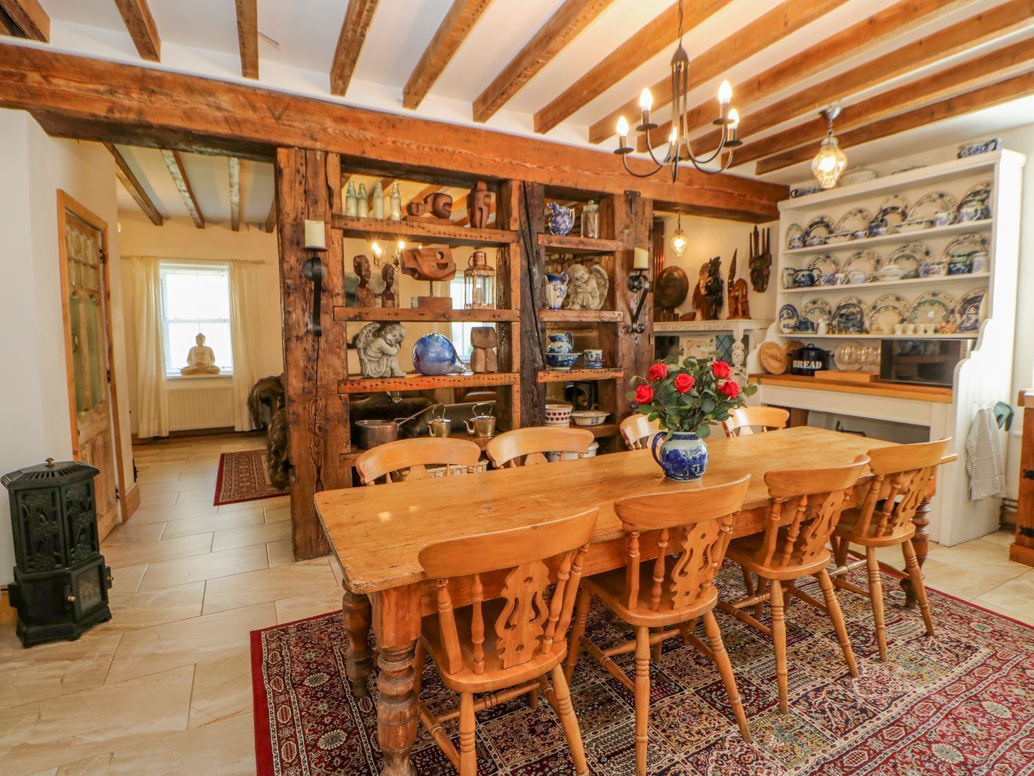 A traditional dining room with a wooden table and chairs, surrounded by shelves with pottery and decorative items.