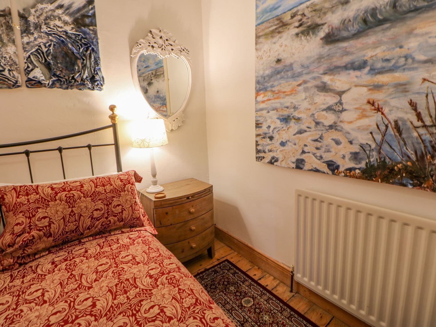 Un dormitorio con cama, mesita de noche, espejo y un cuadro en la pared.