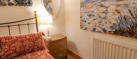Un dormitorio con cama, mesita de noche, espejo y un cuadro en la pared.