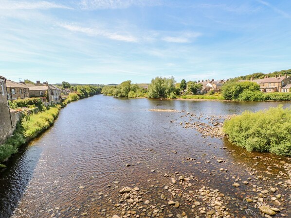 A river with a rocky bank and houses on the opposite side. - Shaftoe Mews (Hexham)