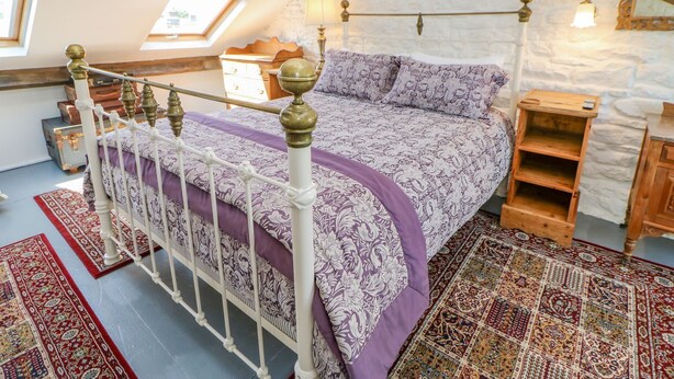 A bedroom with a bed, a wooden dresser, a nightstand, a mirror, and a window with a view of the outside. - Shaftoe Mews (Hexham)
