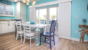 A dining area with a table and chairs, a kitchen with white cabinets, and a view through a glass door. - Sunny 2BR Sanibel Arms West Garden Unit H4 | Lush Escape Near the Beach (Sanibel)