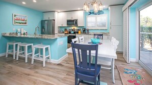 A modern kitchen with a central island, white bar stools, and a dining table with chairs. - Sunny 2BR Sanibel Arms West Garden Unit H4 | Lush Escape Near the Beach (Sanibel)