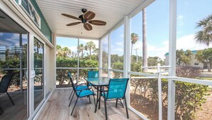 A covered patio with a table and chairs, large windows, and a ceiling fan. - Sunny 2BR Sanibel Arms West Garden Unit H4 | Lush Escape Near the Beach (Sanibel)