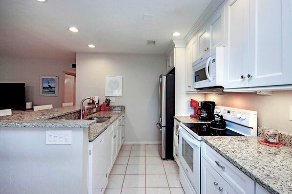 A compact kitchen with white cabinets, a microwave, a stove, and a sink. - Breezy Sanibel Arms West Garden Unit H6 | Short Walk to the Gulf (Sanibel)