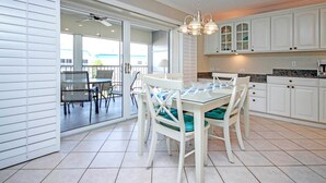 A modern kitchen with white cabinets, a dining area with a glass table and chairs, and a view through the glass door to the outside. - Peaceful Condo with Private Beach Access at Sanibel Arms West (Sanibel)