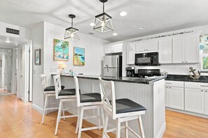 A modern kitchen with white cabinetry, a black countertop, and a central island with bar stools. - Glimpse the Gulf While Relaxing on H8’s Screened Lanai (Sanibel)