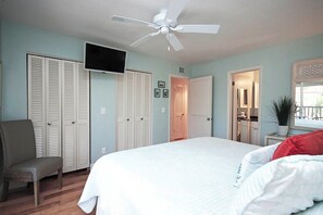 Une chambre à coucher avec un lit, une chaise, un ventilateur de plafond et un téléviseur.