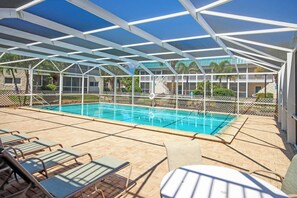 A covered outdoor swimming pool with a safety fence, lounge chairs, and a clear view of the surrounding buildings.