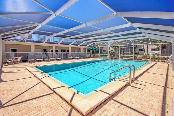 A swimming pool with a covered area, lounge chairs, and a view of the surrounding buildings.