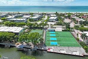 A coastal residential area with multiple buildings, a tennis court, and a dock by the water. - Glimpse the Gulf While Relaxing on H8’s Screened Lanai (Sanibel)