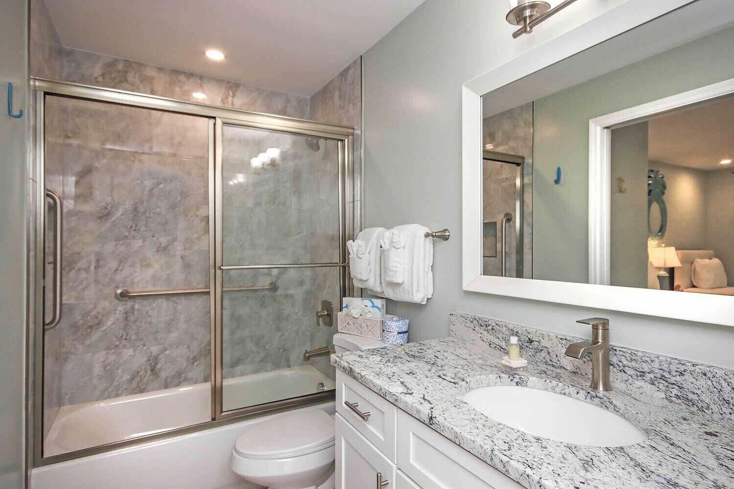 Un baño moderno con ducha de vidrio, lavamanos blanco y un espejo grande.