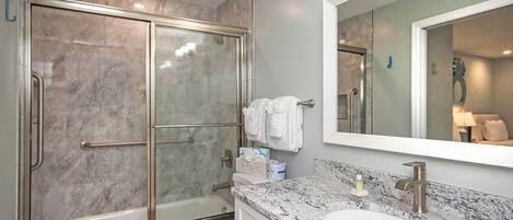 Un baño moderno con ducha de vidrio, lavamanos blanco y un espejo grande.