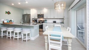 A modern kitchen with white cabinets, a central island with stools, stainless steel appliances, and a chandelier. - Fully Renovated Serene 2/2 ground floor Oasis (Sanibel)