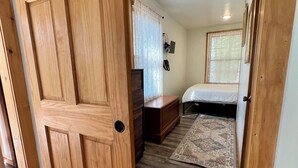 A bedroom with a wooden door, a bed, a desk, and a window with blinds. - Private & Relaxing backyard Hot Tub, Fire pit, nap under the trees in a Hammock (Canadensis)